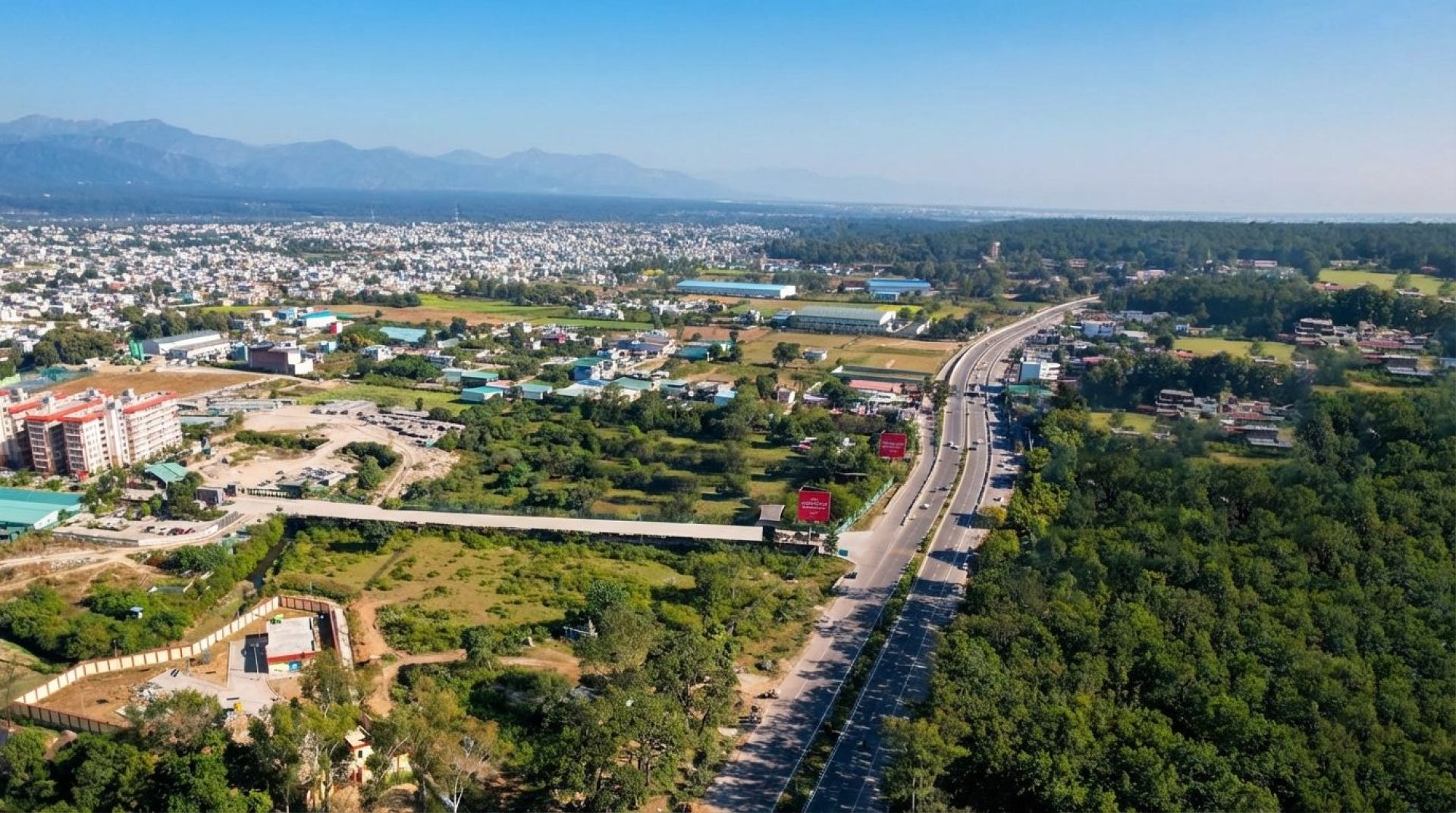 Aerial view of Haridwar Road (NH-72) through green forest on the edge of Dehradun, with the hills behind